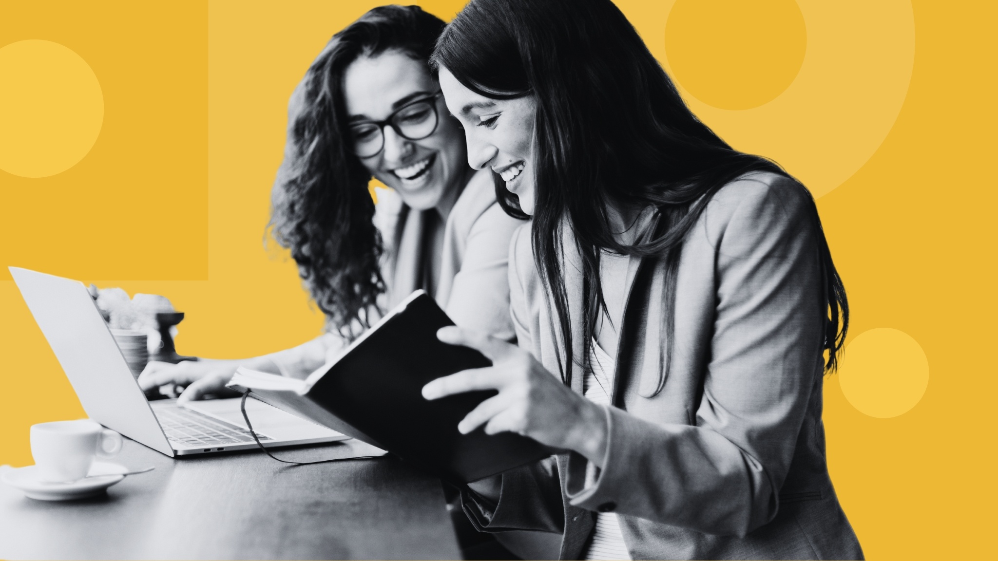 two-women-smiling-transcribing-notes-from-notebook-into-laptop