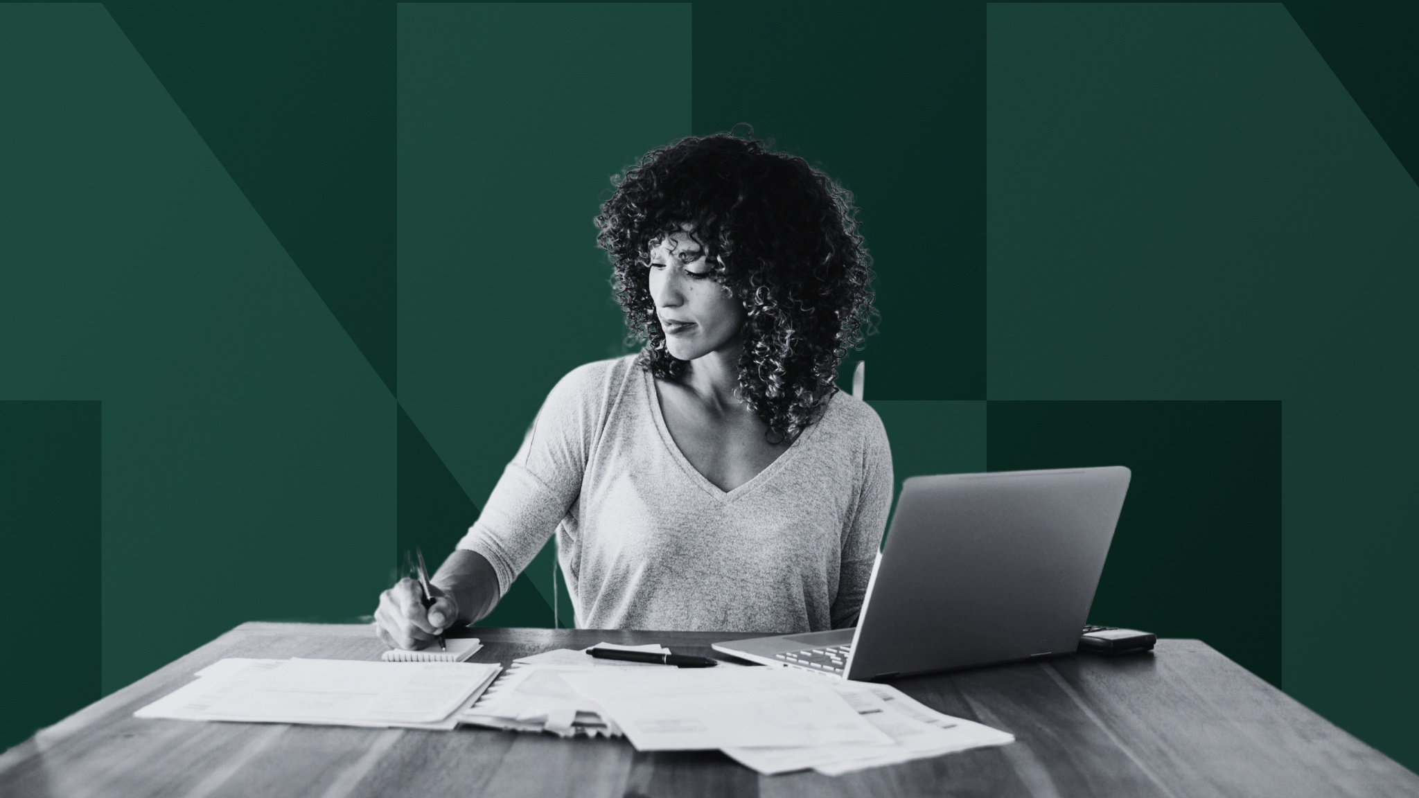 woman-working-at-desk-with-laptop-and-papers-writing-in-notebook